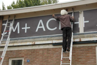 Het ACM+ spandoek wordt aan de loods bevestigd.
